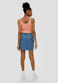 Jupe en denim avec un ourlet effiloché, deux poches arrière et une taille élastique, associée à un débardeur côtelé pêche. Baskets blanches et chaussettes.