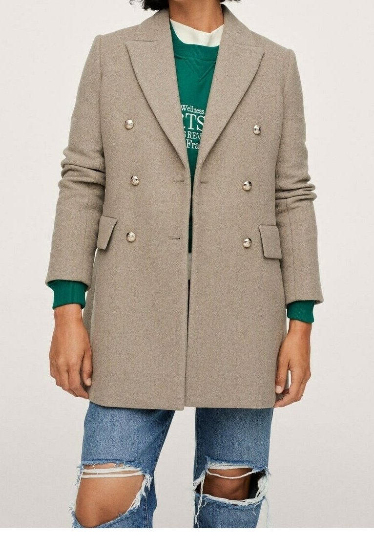 Cappotto doppiopetto grigio chiaro con bottoni argento, design sartoriale e tessuto misto lana. Indossato sopra una felpa verde e jeans blu strappati.