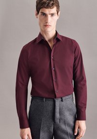 Bordeaux langrugig overhemd met een kraag, voorzien van donkere knopen en een gestreepte binnenkraag, gecombineerd met grijze slim fit broek.