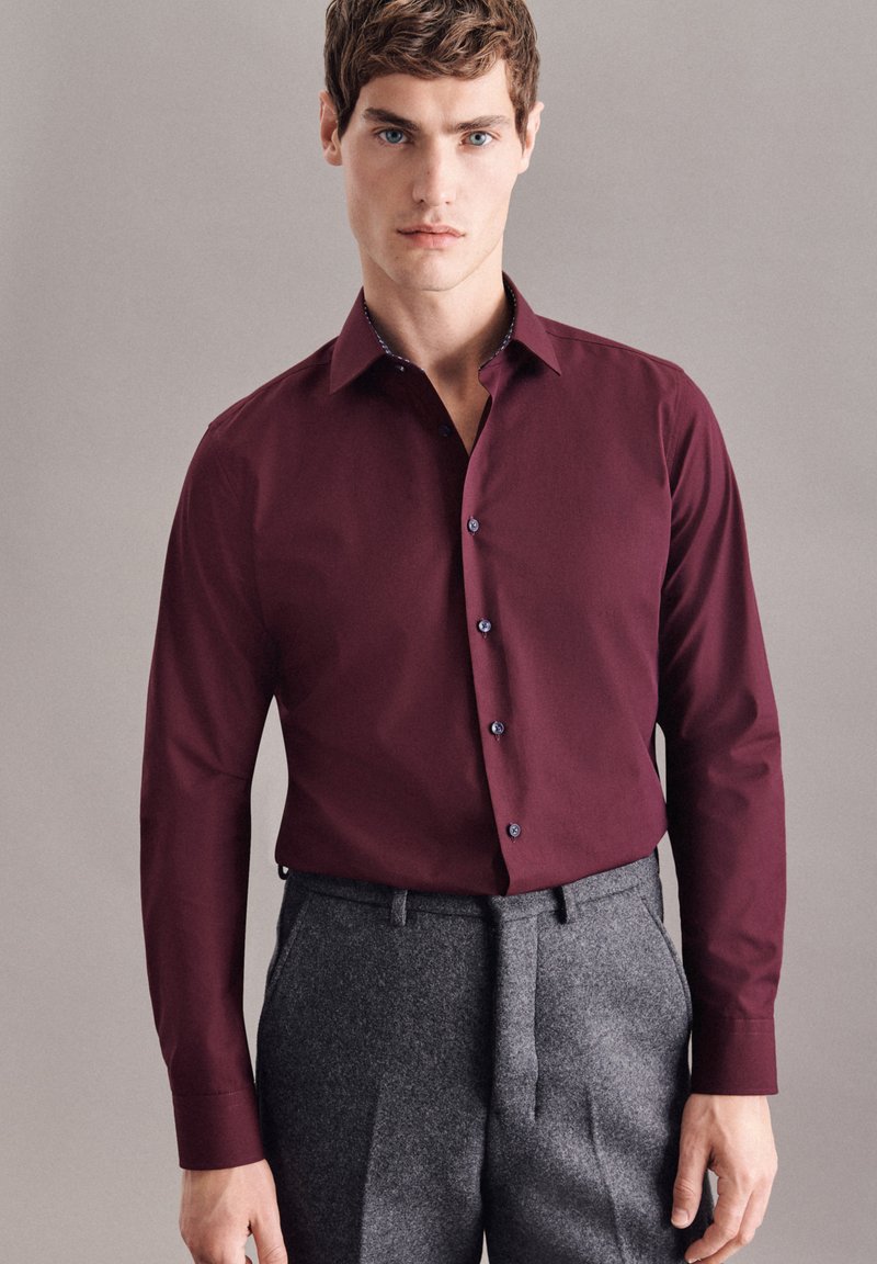 Bordeaux langrugig overhemd met een kraag, voorzien van donkere knopen en een gestreepte binnenkraag, gecombineerd met grijze slim fit broek.