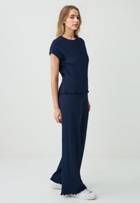 Donkerblauwe tweedelige outfit van textuurstof; korte mouw top met een gekruiste zoom, wijde broek met een vergelijkbare textuur en gegolfde randen.