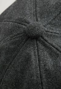 Gray felt cap features a rounded shape with stitched panels and a textured surface. A central fabric-covered button is visible on top.