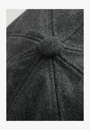 Grau gestrickte Mütze mit einer runden Form, genähten Paneelen und einer strukturierten Oberfläche. Ein zentraler, mit Stoff bezogener Knopf ist oben sichtbar.