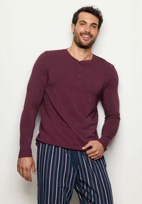 Bordo dlouhý rukáv henley trikotu se třemi knoflíky, spárovaný s námořnickými pruhovanými pyžamovými kalhotami. Hladká textura, volný střih.