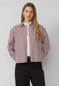 Gestreiftes Button-Down-Hemd in Weinrot und Weiß, mit Kragen, langen Ärmeln und lockerer Passform, kombiniert mit einem weißen Rollkragenpullover darunter.