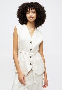 Gilet en lin beige avec un col en V, doté de six boutons noirs, d'une taille ceinturée et de deux poches avant. Texture lisse, design sans manches.