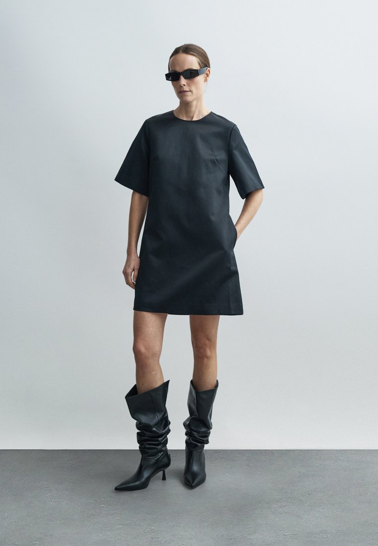 Robe en cuir noir à manches courtes, associée à des bottes noires souples montantes jusqu'au genou. Texture lisse et design minimaliste.