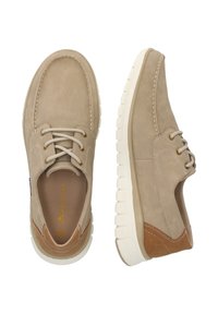 Beige mokkasinikengät, joissa on kirjailtu kuvio, nauhaliukas etuosa ja valkoinen kumipohja. Kengissä on myös ruskeat nahkaosat kantapäällä.