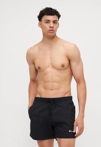 Shorts de bain noirs en matériau léger, dotés d'une taille élastique avec cordon de serrage, et d'un petit logo brodé sur la jambe gauche.
