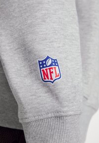 Manica di tessuto grigia con un logo NFL blu, rosso e bianco che presenta un pallone da football e stelle nell'area del polsino.