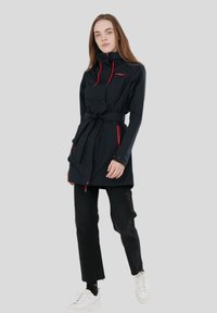 Cappotto impermeabile nero con colletto alto, dettagli rossi e vita con cintura. Presenta tasche con zip e una texture leggera e liscia.