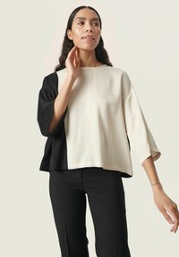 Haut en mélange de coton avec une forme carrée, un design bicolore avec des panneaux noir et crème, et des manches trois-quarts.