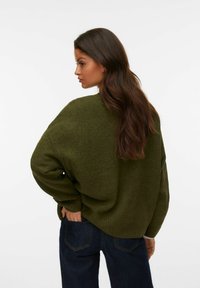 Pull oversized vert olive en maille douce, avec des épaules tombantes et des poignets côtelés, associé à un jean noir.