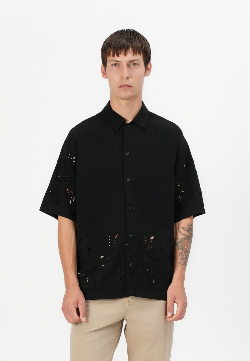 Μαύρο κοντομάνικο πουκάμισο με καπέλο κουμπιού, με κομμένα λουλουδάτα σχέδια στο στρίφωμα και στα μανίκια, κατασκευασμένο από απαλό, ελαφρώς υφασμάτινο ύφασμα.