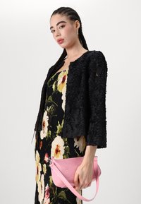 Black textured jacket with floral patterned dress, held with a pink faux leather bag. The ensemble features a mix of colors and intricate designs.
