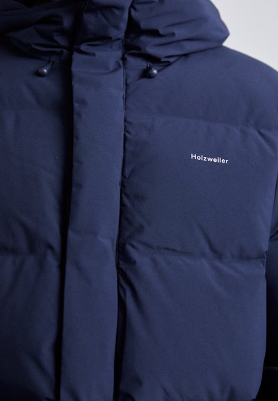 Mörkblå pufferjacka med huva, med en slät textur, horisontellt kviltat mönster och en liten vit logotyp på bröstet.