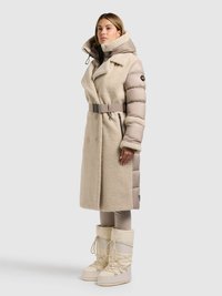 Beige dunjakke med fleecet ydre, bred krave, bælte i taljen og lynlåslommer. Stylet med cremefarvede snestøvler og tætsiddende bukser.