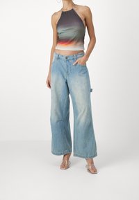 Halterkrátký top v gradientních odstínech zelené a oranžové, spárován s světle modrými širokými džíny. Džíny mají kapsy a volný střih.