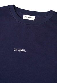 Tamsiai mėlynas marškinėliai su apvaliu kaklu ir balta užrašyta "OH APRIL" tekstu, išsiūtu ant krūtinės, ir atitinkamu audiniu pažymėtu etikete kaklo srityje.