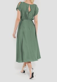 Grön satin midi-klänning med korta ärmar, detalj med nyckelhål på baksidan och en åtsittande midja. Kombinationen med silverfärgade strappy klacksandaler.