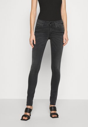 Jeans negros ajustados con una textura suave, cinco bolsillos y detalles de desgastado sutil. Combinados con sandalias negras de tacón.