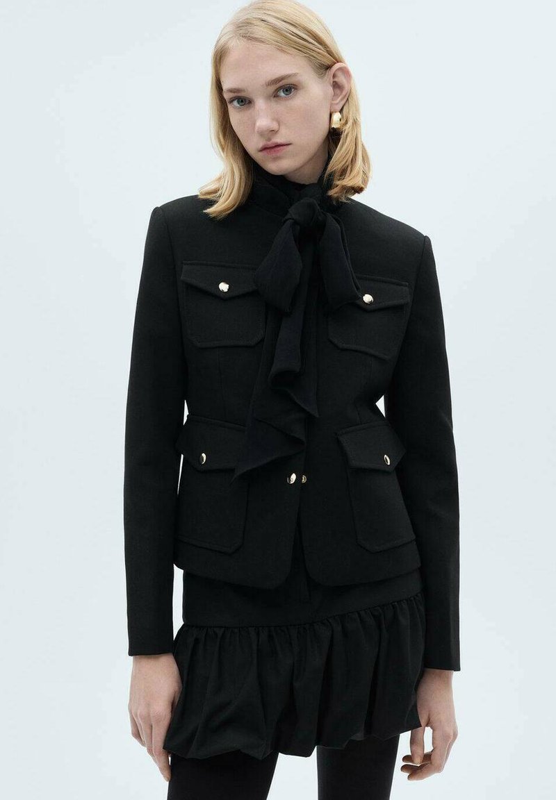 Sacou negru croit, cu detalii aurii, două buzunare în față, o cravată la gât și o margine frotiată. Fabricat dintr-un material structurat cu o textură netedă.