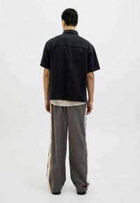 Chemise noire à manches courtes en tissu texturé, associée à un pantalon gris ample avec des rayures crème sur les côtés, vue de dos.
