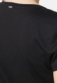 Camiseta negra de manga corta hecha de algodón suave. Presenta una etiqueta de marca sutil cerca del escote y una textura ligera y suave.