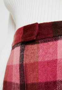Pink and burgundy plaid fabric, featuring a wool texture. A thick waist belt is visible, with neat seams and a smooth finish.