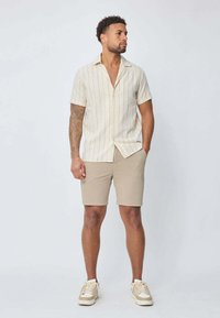 Chemise en lin à manches courtes avec des rayures beige clair et blanches, associée à un short beige et des baskets crème, offrant une coupe décontractée et un col.