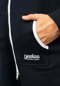 Marinefarbener Zip-Hoodie mit weißen Akzenten, ausgestattet mit einer Brusttasche und gesticktem "geelee"-Logo. Hergestellt aus weichem, strukturiertem Stoff.