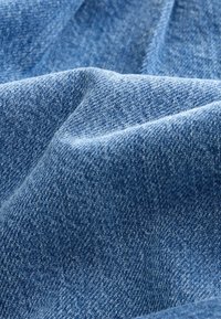 Tela de mezclilla en varios tonos de azul, con un tejido texturizado que presenta patrones de costura visibles y sutiles variaciones de color.