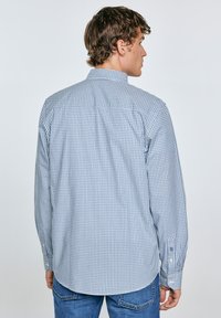 Camisa de manga larga a cuadros en azul y blanco, hecha de algodón, con cuello abotonado y dobladillo curvado, combinada con jeans de mezclilla azules.