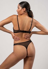 Ensemble de lingerie noire en voile avec un motif à pois. Dispose de bretelles ajustables et d'une fermeture à crochets. Couverture minimale à l'arrière.
