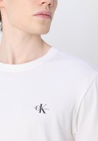 Λευκό βαμβακερό t-shirt με στρογγυλή λαιμόκοψη και μικρό μαύρο λογότυπο Calvin Klein Jeans στο αριστερό στήθος. Λείο υλικό και κλασική εφαρμογή.