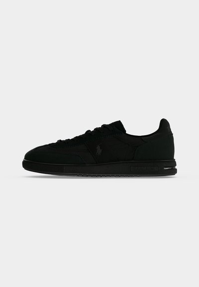 Μαύρο sneaker χαμηλού προφίλ με κορδόνια, λείο πέλμα και διακριτικό λογότυπο στο πλάι και τη φτέρνα, εμφανιζόμενο σε πλάγια όψη σε απλό φόντο.