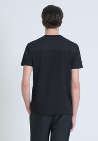 Camiseta negra de manga corta con panel trasero texturizado, cuello redondo y corte recto. La tela parece suave y liviana.
