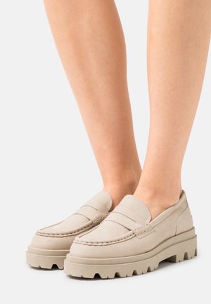 Mocassins beiges avec des semelles en caoutchouc épais, tige en cuir lisse avec des accents cousus et un design de pointe arrondie.