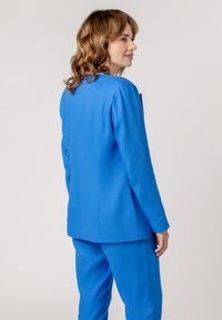 Blue tailored blazer with long sleeves and a smooth texture, paired with matching trousers. Features minimalist design and structured fit.