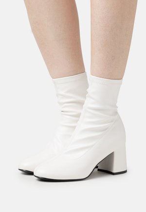 Witte enkellaarzen van glad materiaal, met een slouchy ontwerp, vierkante neus en chunky hak, met contrasterende zwarte zoolaccenten.