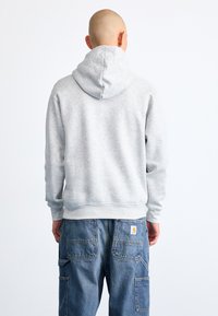 Felpa grigia con cappuccio, realizzata in un tessuto morbido, dotata di un ampio cappuccio e polsini a costine. Abbinata a jeans cargo blu con diverse tasche.