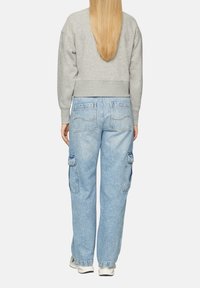 Grijze cropped sweatshirt met lange mouwen, gecombineerd met lichtblauwe cargobroek met grote zijzakken en zichtbare stikseldetails.