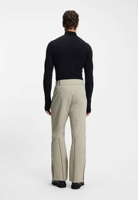 Jasnobeżowe spodnie narciarskie z czarnymi akcentami, o szerokich nogawkach i teksturowanym pasie. Noszone z dopasowaną czarną bluzką z długim rękawem.