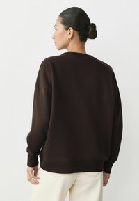 Brun sweatshirt med en avslappnad passform, ribbade ärmslut och nederkant. Baksidan har sänkta axlar och en mjuk, slät tygkvalitet.