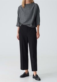 Pantalones negros con pliegues combinados con una blusa texturizada gris que presenta un escote barco y mangas tres cuartos. Mocasines negros completan el conjunto.