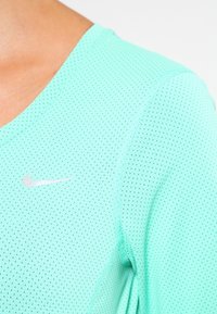 Lys grøn atletisk skjorte lavet af åndbart mesh-stof, med en V-halsdesign og et lille sølvfarvet Nike-logo på brystet.