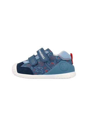 Zapatilla azul marino para niño con patrones de dinosaurios en rojo y azul claro, dos tiras de Velcro, suela blanca y lazo rojo en el talón.