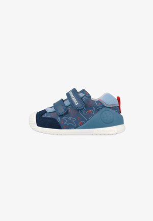 Zapatilla azul marino para niño con patrones de dinosaurios en rojo y azul claro, dos tiras de Velcro, suela blanca y lazo rojo en el talón.