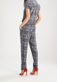 Conjunto de dos piezas que incluye una blusa de manga corta con estampado y pantalones holgados en azul marino y blanco, complementados con sandalias de tacón rojo.
