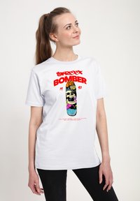 Bílý bavlněný tričko s grafickým designem, na kterém je text "Street Bomber" v červené barvě a barevný skateboard se skull motivem a květinovými prvky.